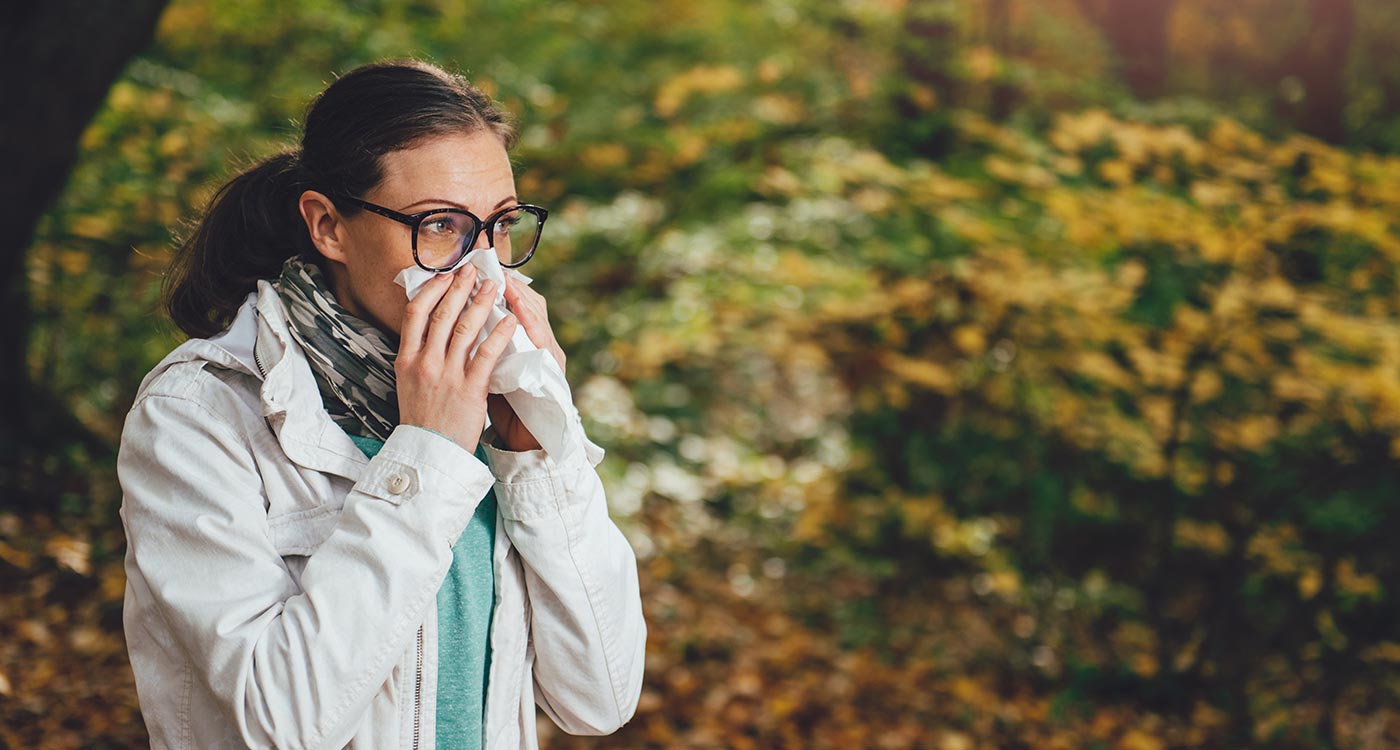 Woman blows her nose while walking outdoors on a nice fall day